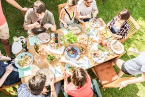 Grillparty in eigenem Garten, Leute sitzen gemeinsam am Tisch und essen und trinken.