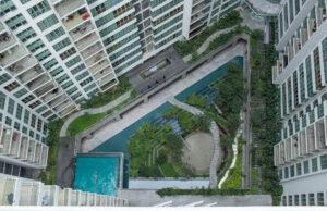 Luftaufnahme eines Mehrfamilien-Hochhauses mit dekorativem grünen Garten und Swimmingpool.