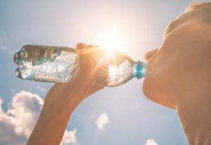 Junge Frau trinkt, bei heißer Sonne, Wasser aus einer Trinkflasche.