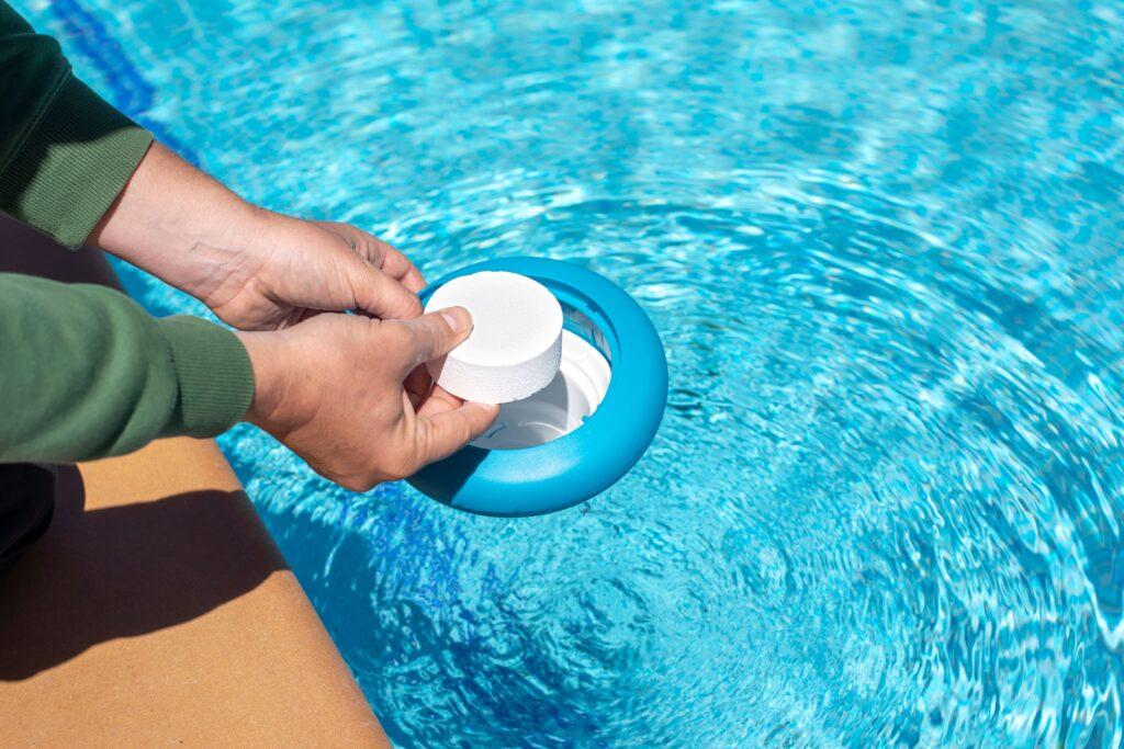 Poolzubehör zur Wasserpflege: Chlortablette wird von Hand in einen Dosierschwimmer im sauberen Pool eingelegt
