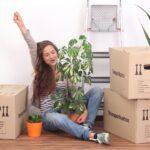 frau sitzt jubelnd zwischen umzugsboxen und pflanzen vor umzug nach beckum